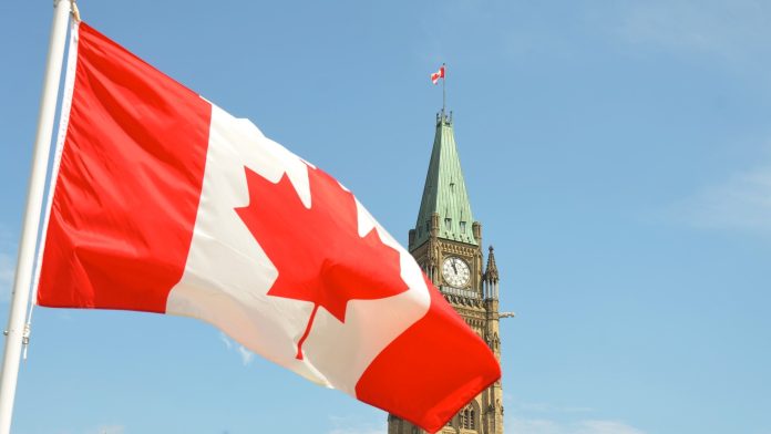 La bandera canadiense desplegada frente a una torre.