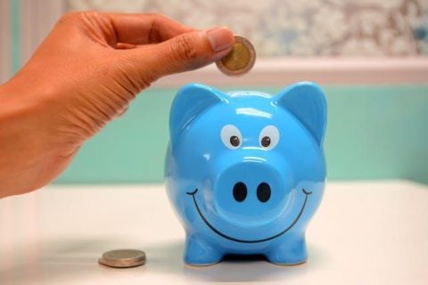 Person steckt Geld in ein blaues Sparschwein